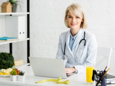 cheerful-blonde-nutritionist-sitting-near-laptop-and-glass-of-fresh-orange-juice.jpg